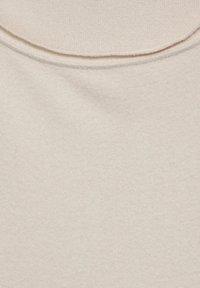 Jasnobeżowa tkanina o gładkiej fakturze, z zaokrąglonym dekoltem i widocznym przeszyciem. Materiał wydaje się miękki i elastyczny.