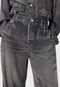 Pantalones de mezclilla negros de cintura alta con cinturilla elástica y cierre de botón, combinados con una chaqueta de mezclilla negra a juego con bolsillos de solapa.