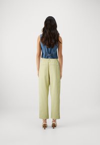 Denimvest med en tettsittende design, parret med lysegrønne, vide bukser. Begge plaggene har enkle linjer og minimal detaljering.