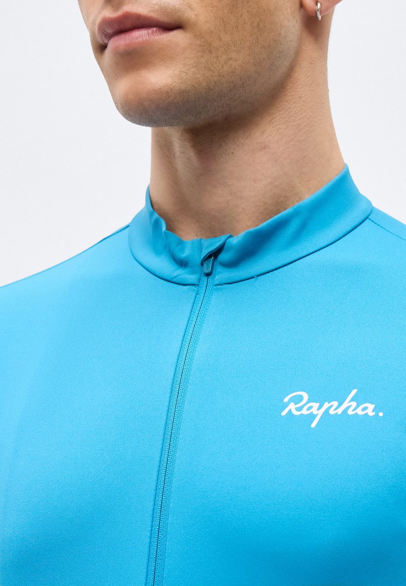 Close-up of a person wearing a zipped bright blue cycling jersey with a small white "Rapha" logo on the chest.