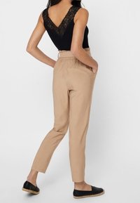 Body nero con pizzo sul retro abbinato a pantaloni beige a sigaretta. La modella indossa espadrillas nere; i pantaloni hanno tasche laterali.