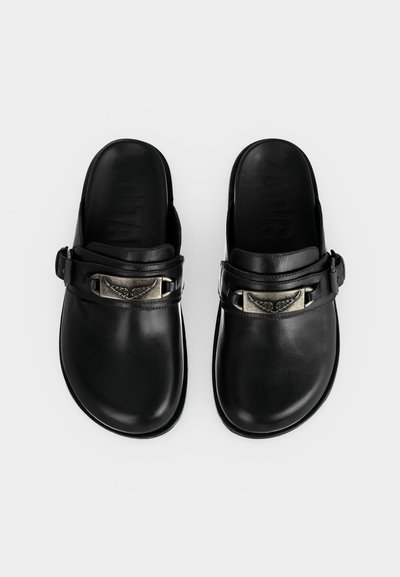 Μαύρα κλαμπόν χωρίς λουράκια με ρυθμιζόμενα λουράκια και μεταλλικά φτερωτά έμβληματα, σε απλό λευκό φόντο.