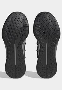 Solados de sapatos atléticos pretos com borracha texturizada, apresentando um padrão de aderência. O design inclui um sulco central e a marca "TRAXION".