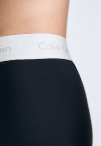 Zwarte katoenen legging met een lichtgrijze elastische tailleband waarop "Calvin Klein" staat gedrukt in een eenvoudige lettertype. Glad textuur, aansluitend ontwerp.