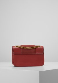 Röd läderhandväska med ett guldkedjestropp, rektangulär form, slät yta, fälllocksstängning och diskreta sömnadsdetaljer på framsidan.