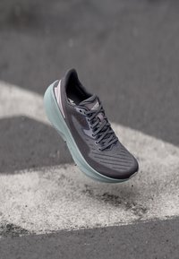 Baskets de sport grises avec un revêtement texturé, un design en mesh et une semelle vert clair, présentant des accents réfléchissants et un système de laçage.