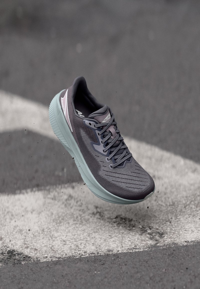 Baskets de sport grises avec un revêtement texturé, un design en mesh et une semelle vert clair, présentant des accents réfléchissants et un système de laçage.