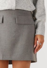 Grauer Wollmischrock mit zwei Vorderseitentaschen, gerader Schnitt und leicht strukturiertem Stoff. Akzentuiert durch einen hellgrauen Strickpullover.