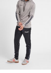 Sudadera gris con detalles negros y patrones en forma de chevron en las mangas, combinada con pantalones deportivos negros con un logo lateral y chevrons a juego.