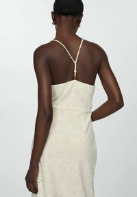 Robe sans manches de couleur crème en tissu texturé avec broderie florale. Présente des bretelles fines et un détail décoratif en perles à l'arrière.