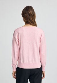 Pullover in maglia rosa chiaro con maniche lunghe, vestibilità rilassata, polsini e orlo a coste, che presenta una texture semplice e liscia e un collo rotondo.