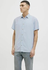 Camisa de manga corta de color azul claro con cierre de botones en el frente, hecha de una tela ligera. Presenta un cuello puntiagudo y un corte relajado.