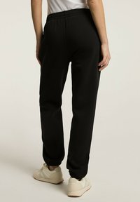 Czarne dresy o luźnym kroju, elastycznym pasie i ściągaczami na kostkach, wykonane z miękkiego materiału. Noszone z jasnymi sneakersami.