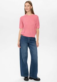 Rosa ribbad stickad topp med korta ärmar, kombinerad med vida blå denimjeans och svarta chunky stövlar. Plaggen har en avslappnad passform och en mjuk textur.