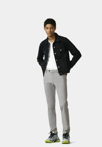 Schwarze Jeansjacke, weißes T-Shirt, hellgraue, schmal geschnittene Hose und schwarze Sneakers mit neongrünen Akzenten. Einfaches Design und lässige Passform.