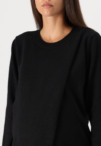 Pull noir avec un col rond et des manches longues, présentant une finition douce et texturée ainsi qu'une coupe décontractée.