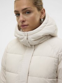 Prešita jakna v svetlo bež barvi z visokim ovratnikom in zapiranjem na sponke. Gladek teksturni vzorec z všitim prešitim tkanjem.