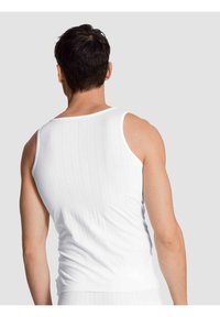 Witte geribbelde tanktop met een klassiek ontwerp, voorzien van dunne schouderbanden en een aansluitende pasvorm. Gladde katoenstof met een gestructureerd oppervlak.