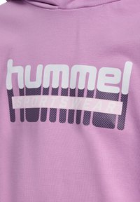 Jasnofioletowa bluza z kapturem. Posiada duże, białe logo "hummel" oraz napis "SPORTSWEAR" w szarych i różowych akcentach. Miękka tekstura materiału.