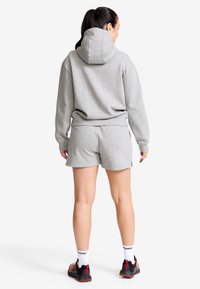 Grå sweatshirt med huva och matchande shorts. Tyget verkar mjukt med en avslappnad passform. Bärs med svarta och röda sneakers, vilket visar vita strumpor.