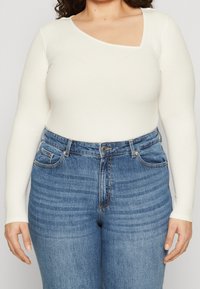 Wit geribd longsleeve shirt met een unieke asymmetrische halslijn, gecombineerd met high-waisted blauwe jeans met een klassieke denimstructuur.