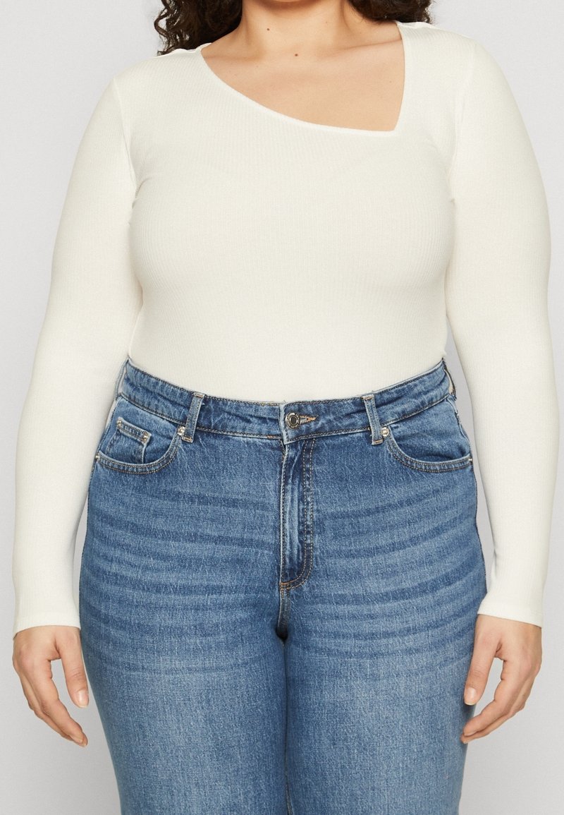 Wit geribd longsleeve shirt met een unieke asymmetrische halslijn, gecombineerd met high-waisted blauwe jeans met een klassieke denimstructuur.
