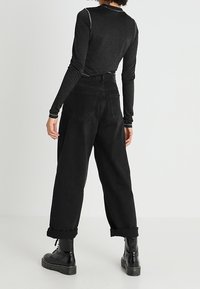 Zwarte langemouwen top met een subtiele glans, gecombineerd met hooggetailleerde, losse zwarte jeans met opgerolde mouwen en zwarte veterboots.