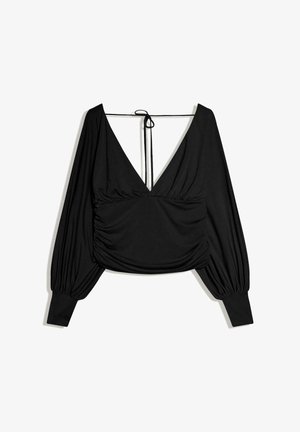 Blouse noire à manches longues et courte, avec un décolleté en V profond, des fronces rassemblées à la taille et une fermeture à nouer au niveau de la nuque.