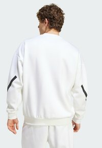 Biele mikina s textúrovaným povrchom, s čiernymi prúžkami na rukávoch a rebrovaným lemom, navrhnutá pre voľný strih.