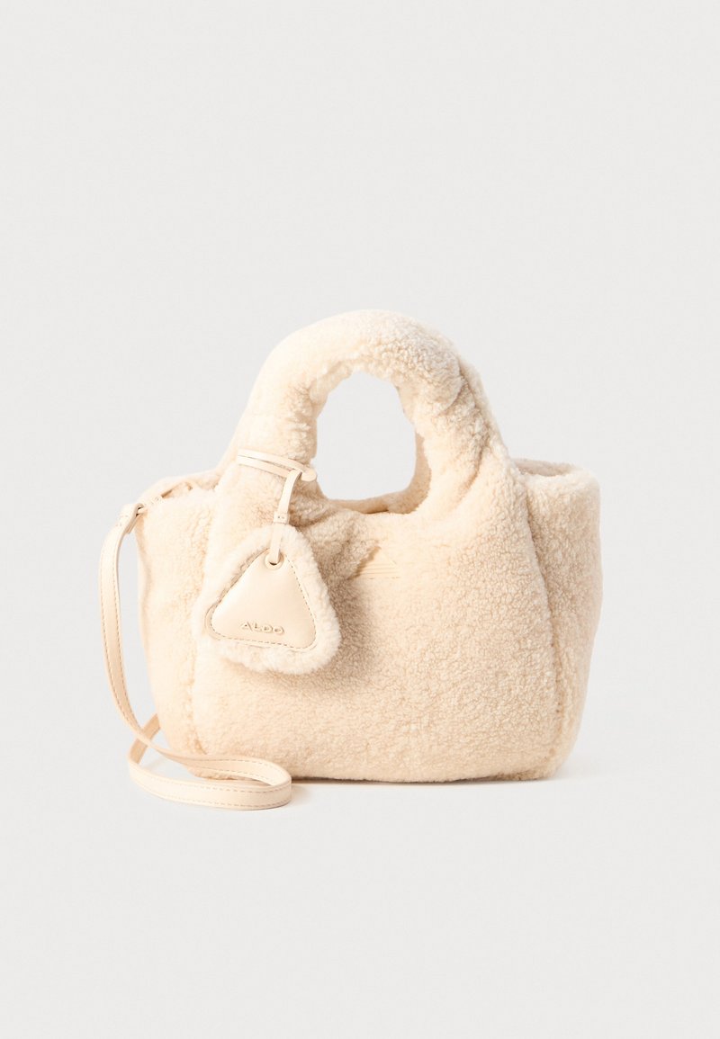 Beige faux shearling håndveske med en lun tekstur, runde topphåndtak, avtagbar skulderreim og et trekantet dekorativt merke.