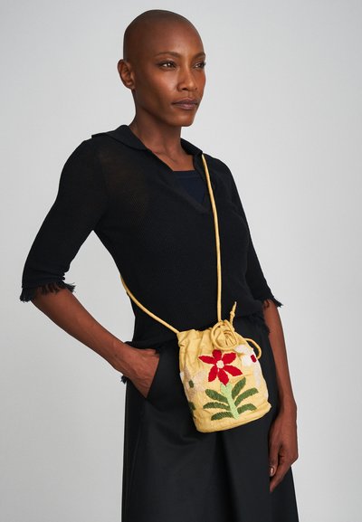 Κίτρινη κεντητή τσάντα με κορδόνι, διακοσμημένη με κόκκινα και πράσινα λουλούδια, φτιαγμένη από υφασμάτινη υφή, φοριέται χιαστί με λεπτό λουρί.
