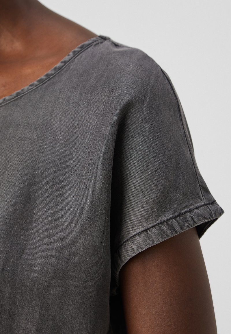 Haut gris à manches courtes fabriqué à partir d'un tissu doux avec une coupe décontractée. Caractéristiques d'un décolleté large et de coutures visibles sur les manches.