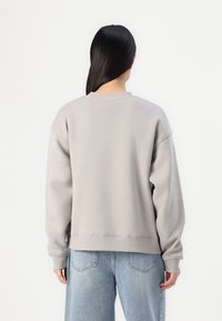 Lysegrå oversized sweatshirt med ribbede mansjetter og kant, med en glatt tekstur. Brukt med lyseblå, løstsittende jeans.