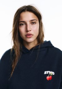 Sötétkék pulóver puha anyagból, elöl két piros cseresznye grafikával és fehér "STWD" felirattal. Klasszikus, kapucnis kialakítás.