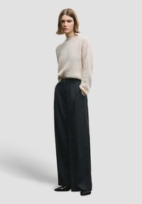 Pull tricoté beige clair à manches longues associé à un pantalon large noir à rayures fines et des chaussures noires à bout pointu.