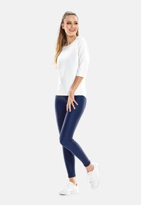 Weißes Oberteil mit drei Viertelärmeln, kombiniert mit dunkelblauen Leggings und weißen Sneakers, in schlanker Passform und glatter Textur.