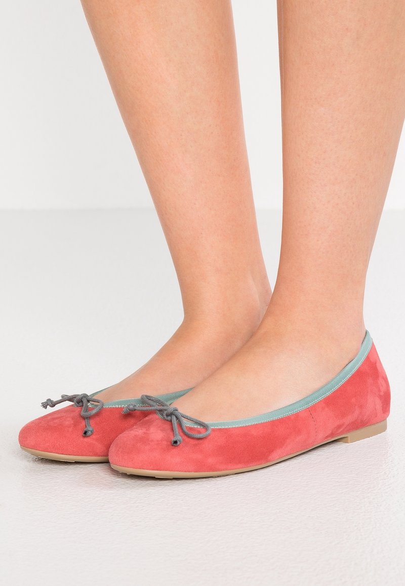 Korallfärgade mockaskor med lätt blå kant och grå rosett. Sulan är platt och skorna har en slät yta.