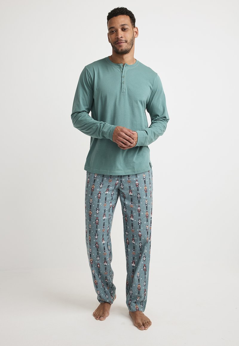 Camisa henley de mangas largas en color turquesa con tres botones, combinada con pantalones de pijama azul claro que presentan patrones de cascanueces y soldados de juguete.