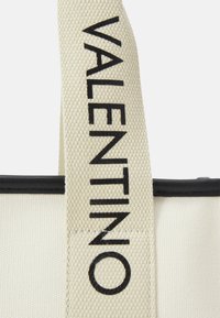Kreemi tooni kangast ostukott musta nahkdetailiga. Kott on varustatud silmapaistva musta "VALENTINO" logoga rihmal. Tekstuuriga pind.