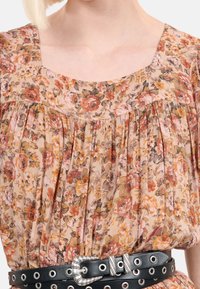 Vestido floral en marrón claro con rosas en tonos rosa y naranja, con pliegues y escote cuadrado; complementado con un cinturón negro con herrajes plateados.