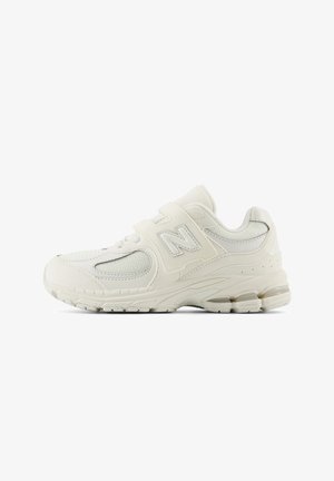 White sports shoes with mesh panels, padded collar, and adjustable velcro straps. Features a textured rubber sole and a subtle logo.