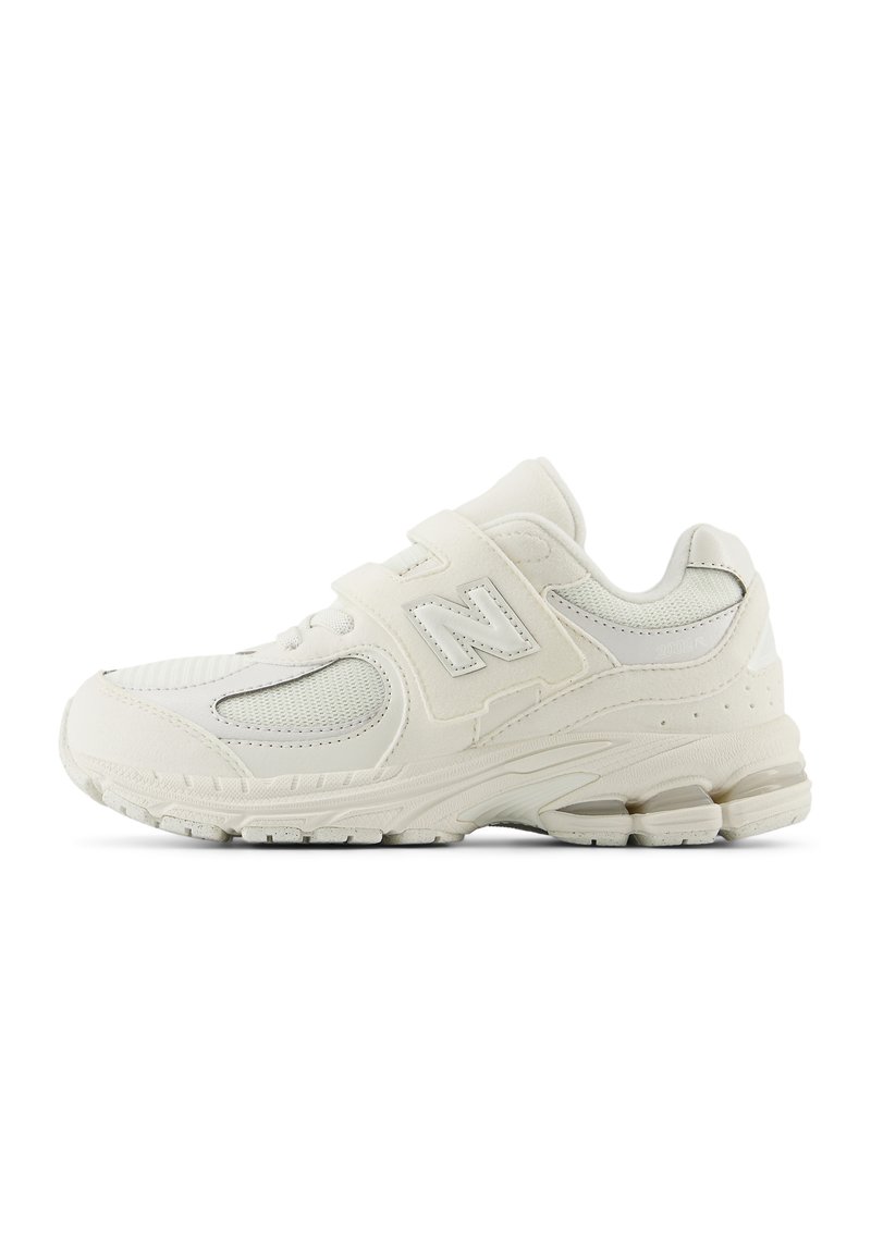 White sports shoes with mesh panels, padded collar, and adjustable velcro straps. Features a textured rubber sole and a subtle logo.