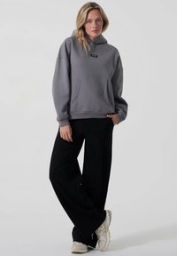 Grå hettegenser med frontlomme, avslappet passform og svart etikett. Sammen med svarte vide bukser og nøytrale joggesko. Enkelt, uformelt design.