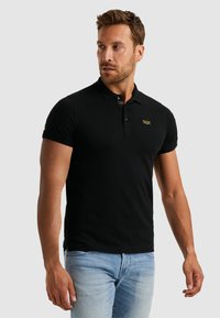 Polo noir en coton, avec un col à trois boutons, des manches courtes et un petit logo sur la poitrine. Conçu avec une coupe ajustée.