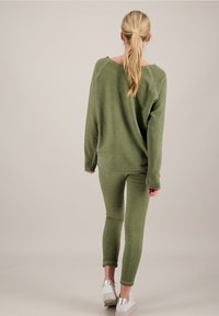 Completo da loungewear verde oliva composto da una maglia a maniche lunghe dal taglio oversized e pantaloni attillati, tutto realizzato in un morbido tessuto testurizzato.