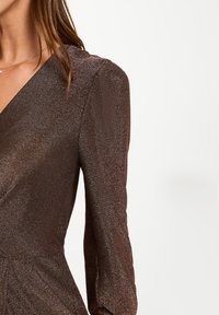 Abito brillante marrone con scollatura a V, maniche lunghe e tessuto testurizzato. Il materiale ha una finitura scintillante, che esalta il suo aspetto elegante.