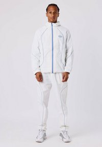Witte tracksuit met blauwe accenten, bestaande uit een leren jack met capuchon en bijpassende broek. Het materiaal lijkt lichtgewicht en glad.