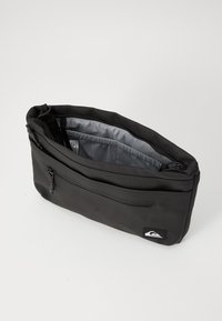 Black, soft-shell pouch bag with a large zippered opening, front pocket, and gray interior lining. Features branded logo on side.