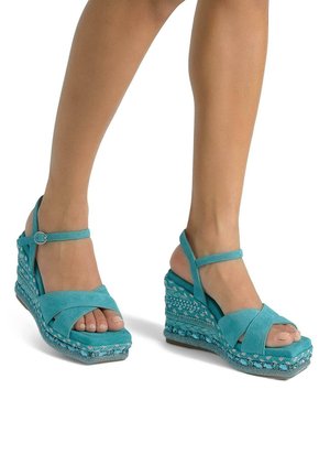Sandalias de cuña turquesa con tiras cruzadas, punta abierta y correa en el tobillo. Plataforma de tejido texturizado con acentos decorativos en la base.