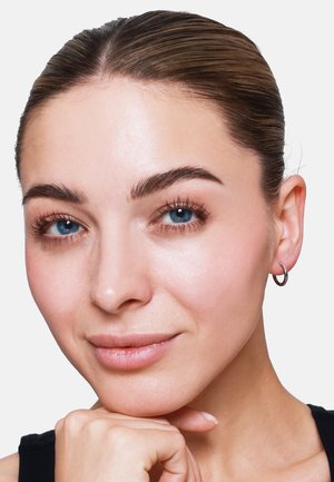 Nahaufnahme eines Gesichts mit glatter Haut, geraden dunklen Haaren, blauen Augen und einem kleinen silbernen Ohrstecker. Einfache, natürliche Make-up.